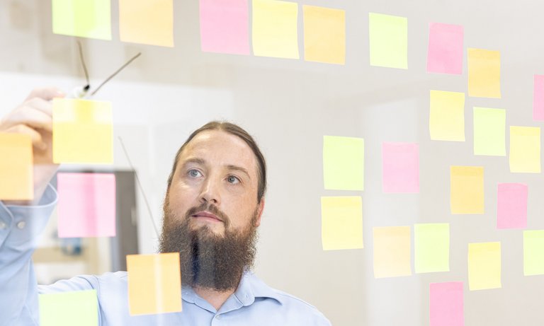 Entwickler an Glastafel. Entwickler ordnet Post-its an einer Glastafel.