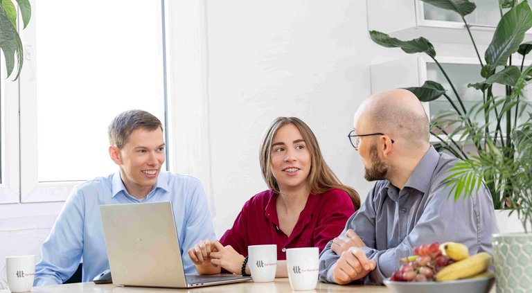 Mitarbeitende diskutieren über Förderprojekte Drei Mitarbeitende diskutieren über Förderprojekte an einem Tisch